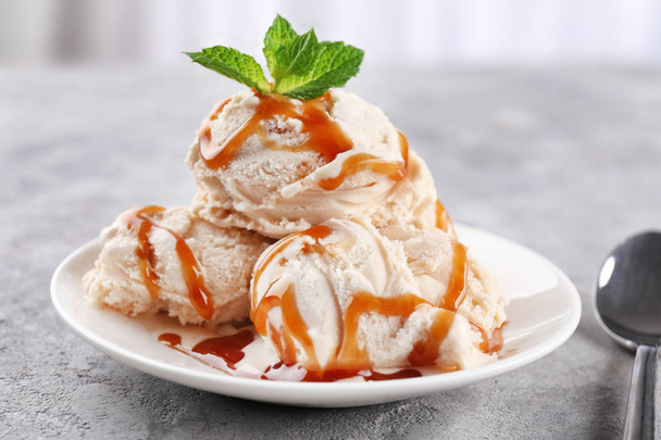 Plate of delicious ice cream with caramel topping on table - Fotó, kép