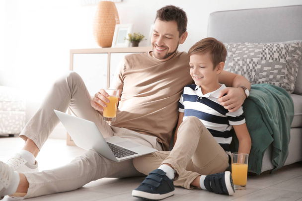 Cute little boy and father with laptop sitting on floor at home - Foto, Imagen