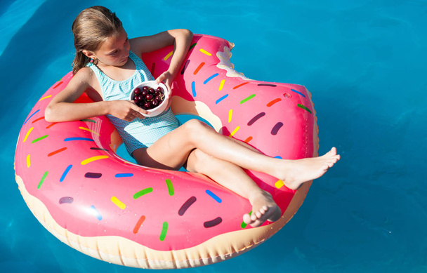 Mädchen sitzt auf einem bunten aufblasbaren Donut mit Kirschen - Foto, Bild