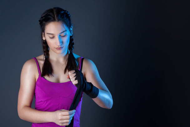 Female boxer is wrapping hands with black boxing wraps. Isolated on dark background with space for text - Photo, Image