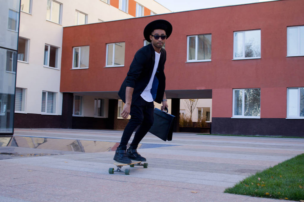 Concept of young,fast and mobile manager. Funny buisinessman on skateboard in black suit. - Fotografie, Obrázek