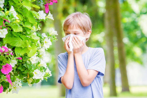 Allergy. Little boy is blowing his nose near blossoming flowers - Photo, Image