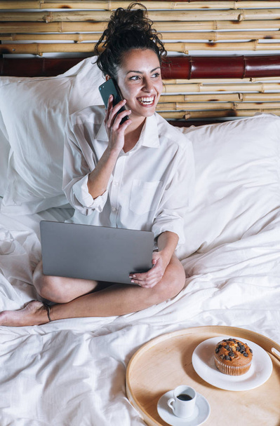 Pretty woman with phone and laptop in bed - Fotó, kép