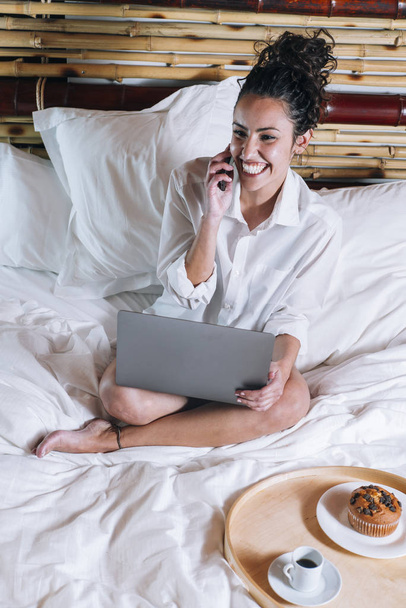 Pretty woman with phone and laptop in bed - Foto, imagen