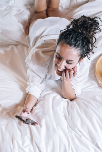 Pretty woman with phone in bed - Foto, afbeelding