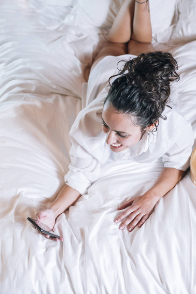Pretty woman with phone in bed - Foto, afbeelding