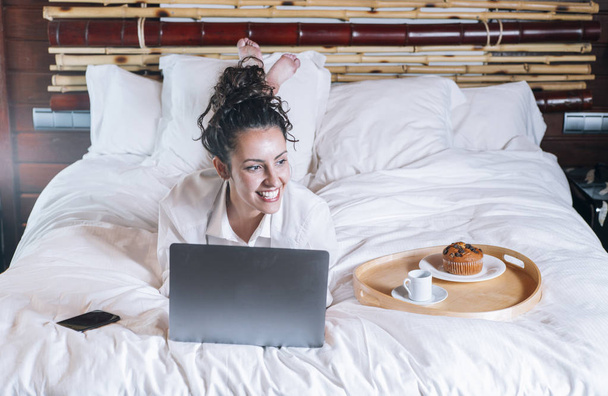 Красивая женщина с телефоном и ноутбуком в постели
 - Фото, изображение