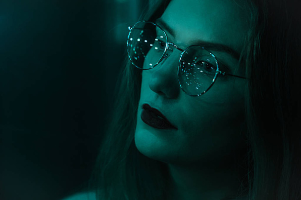 Portrait of a fashion beautiful white girl with glasses in the dark and bokeh Green tinted effect of faded film. Effect of the focus of the low intensity of sharpness. - Fotografie, Obrázek