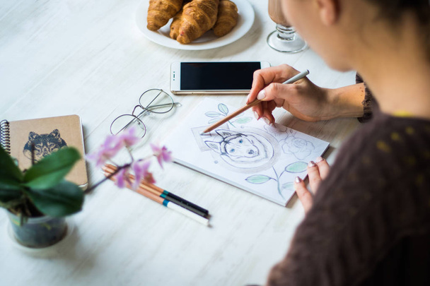 Dívka je obraz s tužky Husky na bílém listu v kavárně na světlém pozadí bílý dřevěný stůl - Fotografie, Obrázek