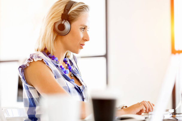 Young woman in the office with headphones - Фото, изображение