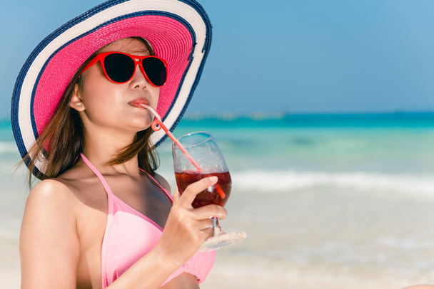 Lifestyle happy young adult asian woman in pink bikini with cocktail in hand and straw hat on beach. Lifestyle outdoors woman portrait. Lifestyle woman summer concept. - Foto, Bild