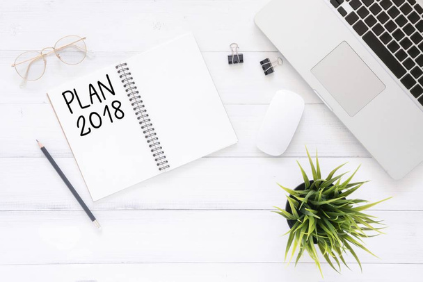 Minimal work space - Creative flat lay photo of workspace desk with Plan 2018 New Year list notebook and laptop on wooden background. Top view flat lay photography. 2018 happy new year concept. - Photo, Image