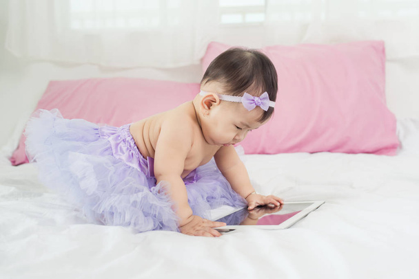 Γλυκό μωρό κορίτσι που κάθεται στο κρεβάτι στο σπίτι με ψηφιακό tablet - Φωτογραφία, εικόνα