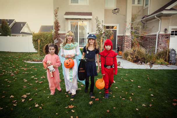 Grupo de niños vestidos con disfraces de Halloween que van a engañar o tratar al aire libre en octubre en un barrio decorado
 - Foto, Imagen