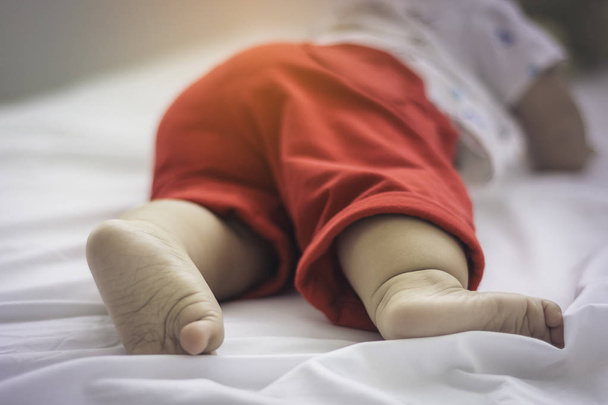 Close-up of a baby foot which wore red cotton trousers while a white lie on the mattress. - Foto, Imagem