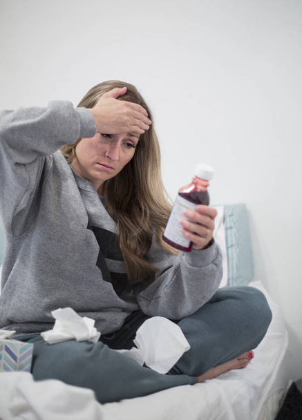 Женщина с простудой, глядя на этикетку таблетки или пузырька с лекарствами
 - Фото, изображение