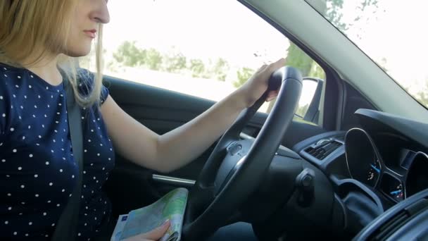 Zeitlupenaufnahmen einer jungen Frau, die Auto fährt und auf eine Landkarte aus Papier blickt. Autofahrerin verirrte sich auf unbekannter Straße - Filmmaterial, Video