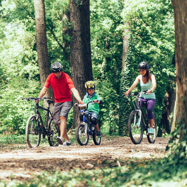Cheerful family biking together in park - Photo, Image