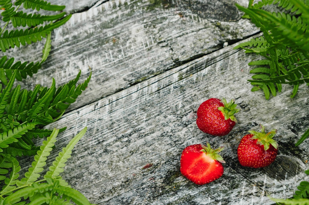 Strawberries on a wooden gray table on a green background, leaves of paparatnik, strawberry season. opy space for text, - 写真・画像
