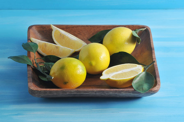 group of yellow lemons with leaves on a square wooden plate  - Foto, Imagen