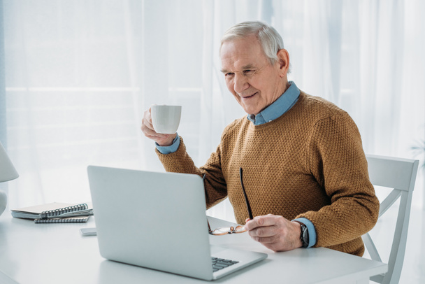 Senior homme confiant travaillant sur ordinateur portable et tenant tasse de café
 - Photo, image