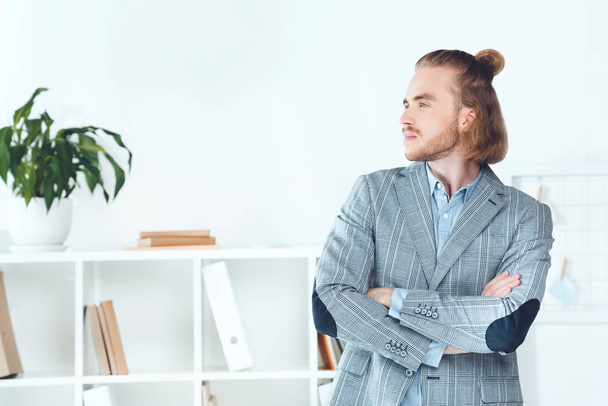handsome businessman standing in office with crossed arms and looking away - Foto, afbeelding