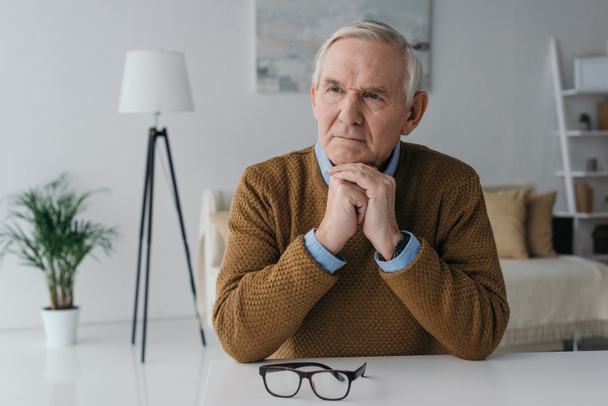 Senior thoughtful man sitting by the desk in light room - Photo, Image
