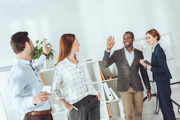 smiling multicultural businesspeople waving hands in office - Foto, Imagem