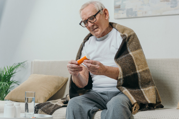 Senior man in eyeglasses and plaid looks at pill bottle - Valokuva, kuva