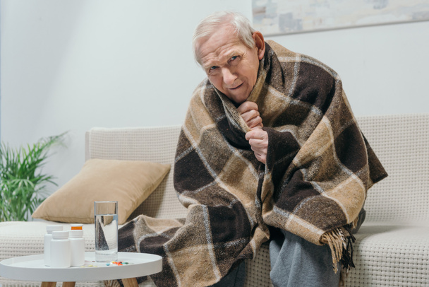 Senior chilled man covered in plaid with medications on table - Photo, Image