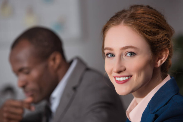 Valkoihoinen nainen hymyilee kameralle toimistotiloissa
 - Valokuva, kuva