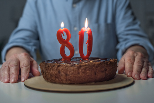 Close-up view of senior man celebrating 80 anniversary with cake and burning number candles - Foto, Imagem