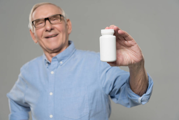 Senior luottavainen mies pitää valkoinen pullo pillereitä eristetty harmaalla pohjalla
 - Valokuva, kuva