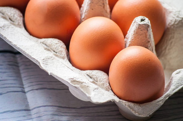 Крупный план сырых куриных яиц в яичной коробке на белом деревянном фоне - Фото, изображение