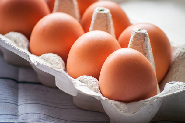 Крупный план сырых куриных яиц в яичной коробке на белом деревянном фоне - Фото, изображение