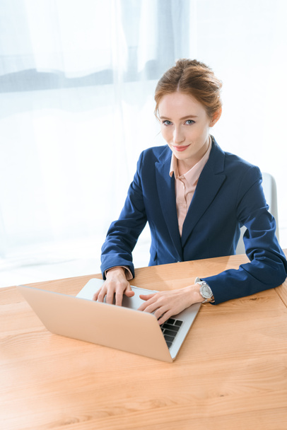 smiling caucasian woman using laptop while looking at camera at office space  - Foto, immagini