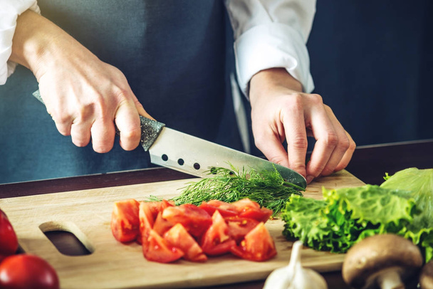 Lo chef in grembiule nero taglia verdure. Concetto di prodotti ecologici per cucinare
 - Foto, immagini
