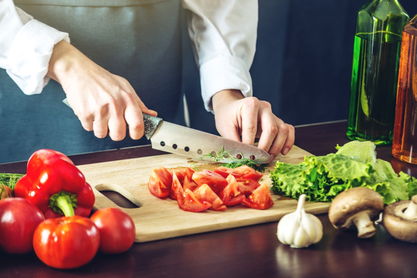 De chef-kok in zwarte schort snijdt groenten. Concept van eco-vriendelijke producten voor het koken - Foto, afbeelding