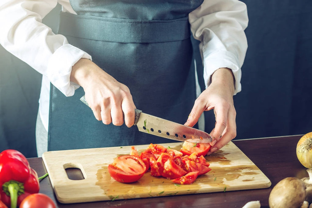 Lo chef in grembiule nero ha tagliato i pomodori. Concetto di prodotti ecologici per cucinare
 - Foto, immagini