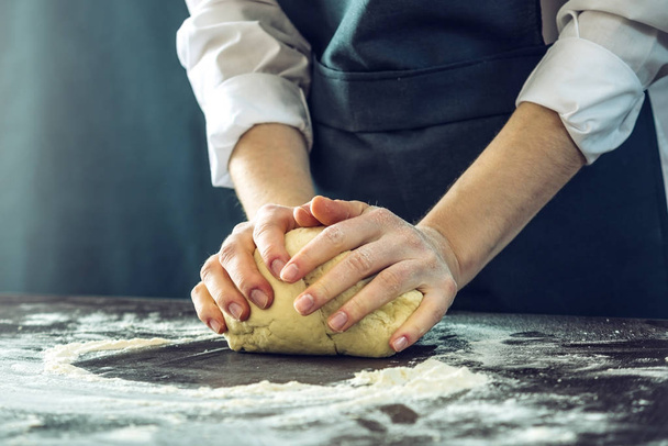 Lo chef in grembiule nero fa la pasta della pizza con le mani sul tavolo
 - Foto, immagini