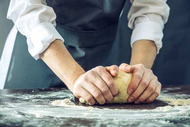 Шеф-кухар в чорному фартусі робить тісто для піци своїми руками на столі
 - Фото, зображення