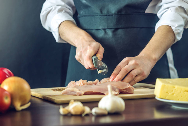 Lo chef in grembiule nero taglia coltello filetto di pollo. Concetto di prodotti ecologici per cucinare
 - Foto, immagini