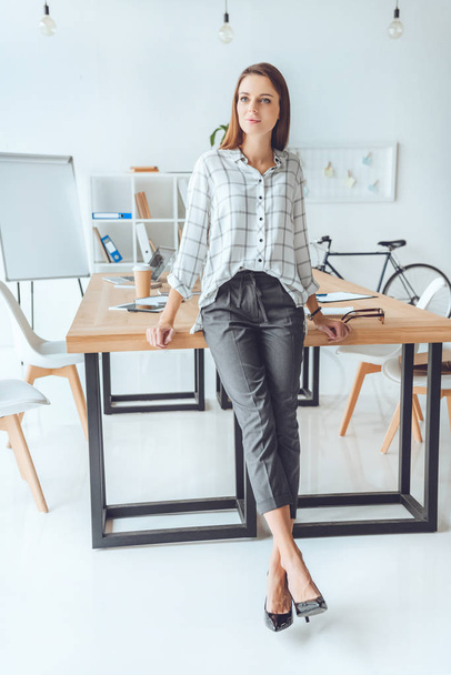woman in shirt leaning on table and looking away at office space  - Photo, Image