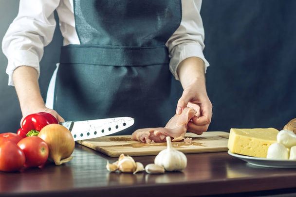 Siyah önlük Şef tavuk fileto bıçağı keser. Yemek pişirmek için çevre dostu ürünler kavramı - Fotoğraf, Görsel