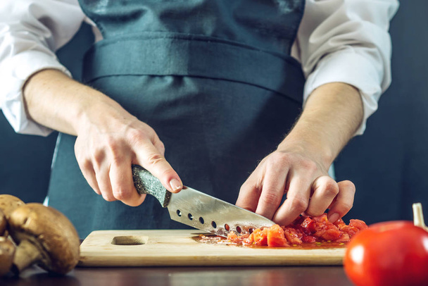 Kokki mustassa esiliinassa leikkasi tomaatit. Ympäristöystävällisten ruoanlaittotuotteiden käsite
 - Valokuva, kuva