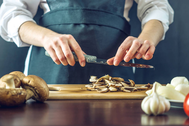 The chef in black apron cuts mushrooms with a knife. Concept of eco-friendly products for cooking - Φωτογραφία, εικόνα