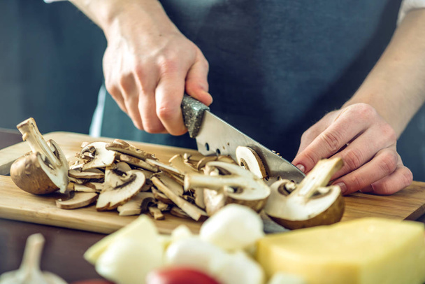 The chef in black apron cuts mushrooms with a knife. Concept of eco-friendly products for cooking - Photo, Image