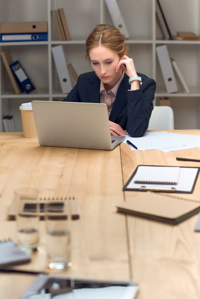 Femme pensive assise à table et regardant sur un ordinateur portable
 - Photo, image