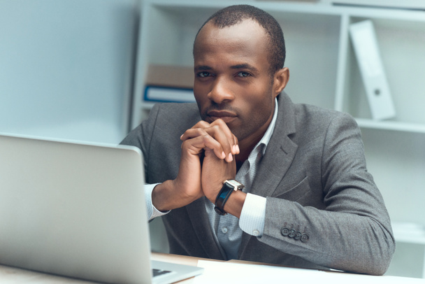 pensive african man sitting at table with laptop at office space - Zdjęcie, obraz
