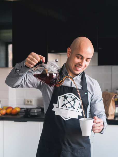 Bald happy man on apron with teapot at kitchen - Fotoğraf, Görsel